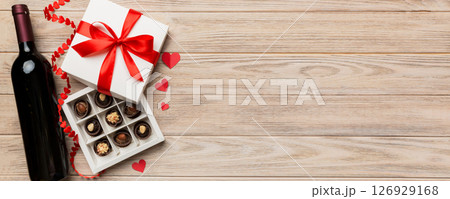 Bottle of red wine on colored background for Valentine Day with gift and chocolate. Heart shaped with gift box of chocolates top view with copy space 126929168