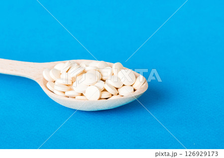 Heap of white pills on colored background. Tablets scattered on a table. Pile of red soft gelatin capsule. Vitamins and dietary supplements concept Heap of white pills on colored background. Tablets scattered on a table. Pile of red soft gelatin capsule. Vitamins and dietary supplements concept 126929173