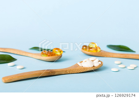 Vitamin capsules in a spoon on a colored background. Pills served as a healthy meal. Red soft gel vitamin supplement capsules on spoon 126929174
