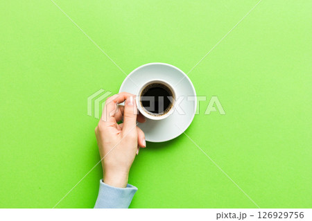 Minimalistic style woman hand holding a cup of coffee on Colored background. Flat lay, top view cappuccino cup. Empty place for text, copy space. Coffee addiction. Top view, flat lay 126929756