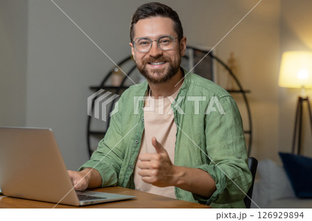 Man sitting at desk working on laptop showing thumb up like gesture 126929894