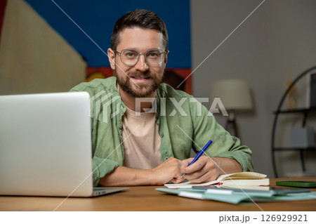 Bearded man working on laptop in home office setup 126929921