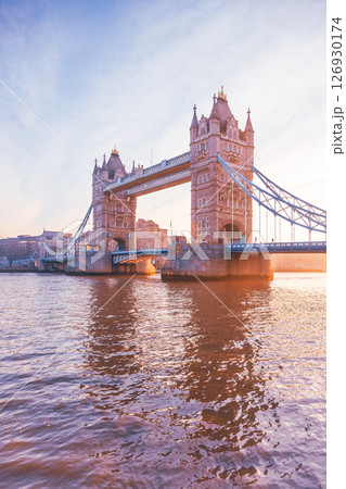 Tower Bridge stands majestically as the sun rises, casting warm hues over the Thames River. This iconic landmark is illuminated, showcasing its architectural beauty at dawn. 126930174