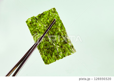 Chopsticks hold a piece of crispy dried seaweed. Nori, Japanese edible seaweed. Chopsticks hold a piece of crispy dried seaweed. Nori, Japanese edible seaweed. 126930320