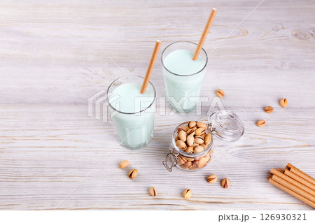 Pistachio milk in glasses with paper straws, nuts in jar on wooden background. 126930321