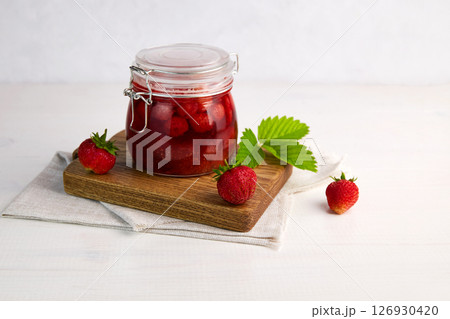 Strawberry jam in a glass jar with fresh berries on white wooden background. 126930420