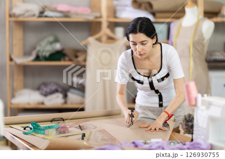 Female clothing designer cutting pattern paper in tailoring studio Female clothing designer cutting pattern paper in tailoring studio 126930755