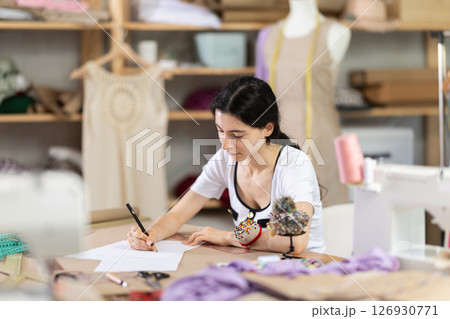 Female fashion designer sketching new clothing ideas in sewing studio Female fashion designer sketching new clothing ideas in sewing studio 126930771
