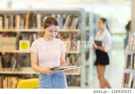 Young female student stands in library with stack of books 126930831