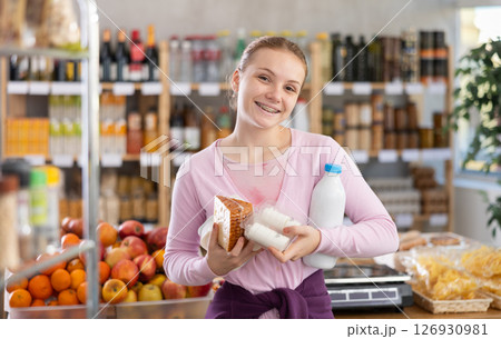 Female shopper with various dairy products in her hands continues to make choice in grocery department of supermarket Female shopper with various dairy products in her hands continues to make choice in grocery department of supermarket 126930981