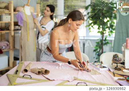 Female tailor cutting fabric while teammate working with mannequin Female tailor cutting fabric while teammate working with mannequin 126930982