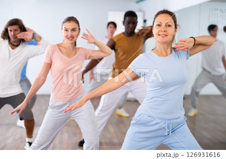 Group of sporty young adult multinational sports people making straight line with hands exercising dancing in gym 126931616