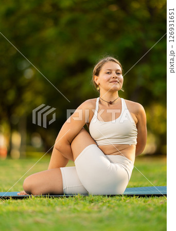 Girl in park on green grass of lawn performs lord of fishes, Matsyendrasana 126931651