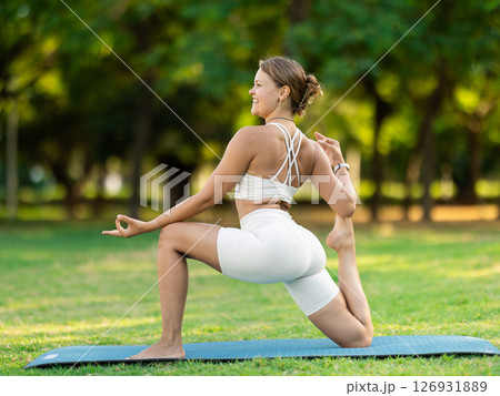Young yogini performing Crescent Low Lunge Pose in summer park Young yogini performing Crescent Low Lunge Pose in summer park 126931889