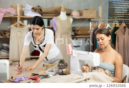 Young seamstresses stitching and drafting paper patterns in workshop 126932088