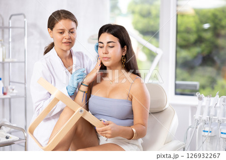 Cosmetologist explaining facial procedure to young girl looking in mirror Cosmetologist explaining facial procedure to young girl looking in mirror 126932267