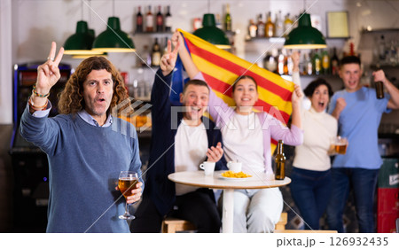 Excited sports supporters of different ages with flag of Estelada, rejoicing winning game with beer and snacks in pub Excited sports supporters of different ages with flag of Estelada, rejoicing winning game with beer and snacks in pub 126932435