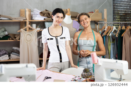 Two young female tailors standing in modern sewing studio Two young female tailors standing in modern sewing studio 126932444
