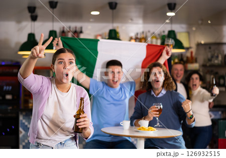 Emotional young adult sports fans waving Italian flag while drinking beer and watching game match together in bar Emotional young adult sports fans waving Italian flag while drinking beer and watching game match together in bar 126932515