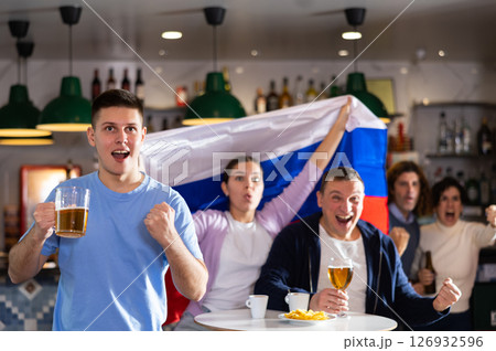 Group of excited young adult friends waving flag of Russia and supporting national team with beer in bar 126932596