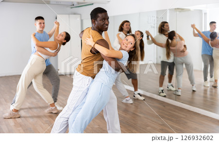 Positive middle-aged male partner leading young female in pair dancing during class together in studio 126932602