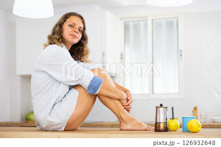 Portrait of attractive woman sitting on kitchen table Portrait of attractive woman sitting on kitchen table 126932648