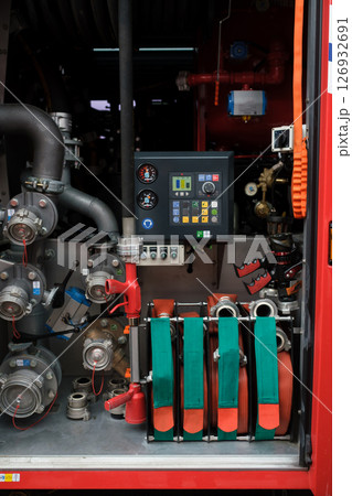 Equipment used for firefighting is neatly organized in a fire truck compartment with hoses, valves, and control panels present in the background during daylight hours Equipment used for firefighting is neatly organized in a fire truck compartment with hoses, valves, and control panels present in the background during daylight hours 126932691