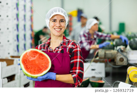 Happy Hispanic workwoman holding half of watermelon standing near fruit sorting line Happy Hispanic workwoman holding half of watermelon standing near fruit sorting line 126932719
