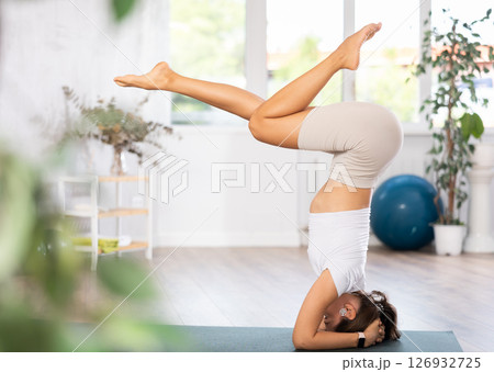 Young woman yoga trainer performing forearm stand pose on black rug 126932725