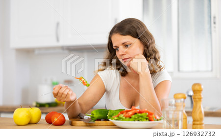 Sad woman eating vegetable salad in kitchen 126932732