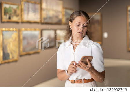 Woman with phone in hands view pictures and icons in museum hall Woman with phone in hands view pictures and icons in museum hall 126932746