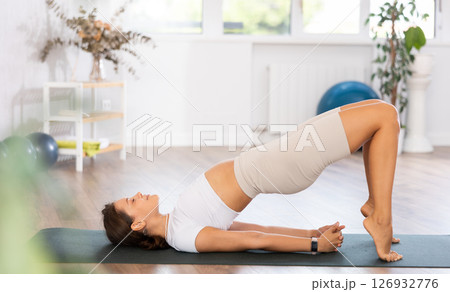 Young woman yoga trainer performing bridge pose on black rug Young woman yoga trainer performing bridge pose on black rug 126932776