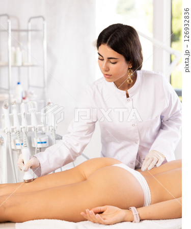 Cosmetologist performing ultrasound liposuction on posterior thighs of female client Cosmetologist performing ultrasound liposuction on posterior thighs of female client 126932836