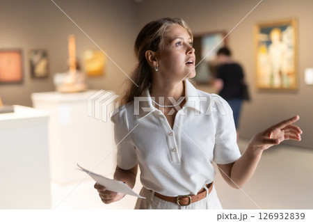 Woman with sheet piece of paper in hands view pictures and icons in museum hall Woman with sheet piece of paper in hands view pictures and icons in museum hall 126932839