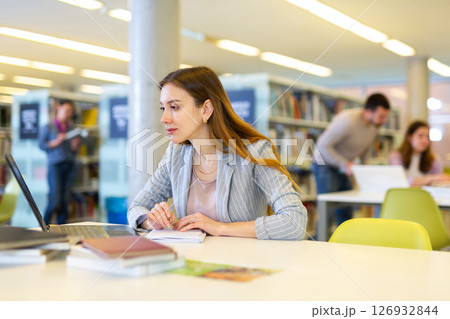 Female student with laptop and books in public library 126932844