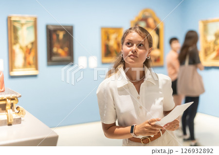 Woman with sheet piece of paper in hands view pictures and icons in museum hall 126932892