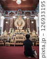 A woman is sitting in front of a golden Buddha statue in a temple. 126933195
