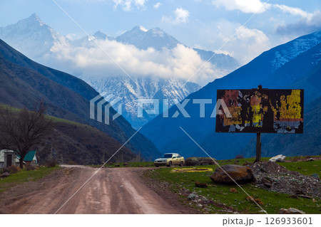 Car parked on rural road with mountains and old decayed billboard in Kyrgyzstan 126933601
