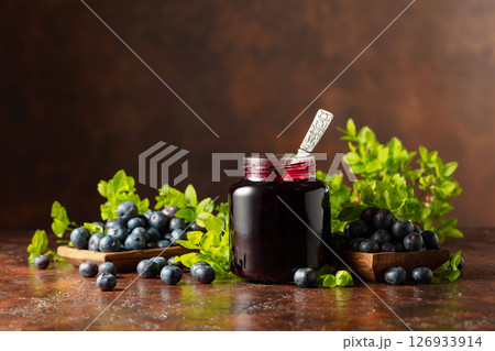 Blueberry jam and fresh berries on a brown background. Blueberry jam and fresh berries on a brown background. 126933914