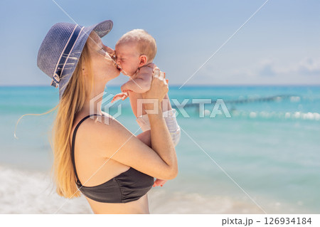 Mother holding her newborn baby by the turquoise sea, sharing a peaceful and loving moment. Family bonding, motherhood, and travel with baby concept Mother holding her newborn baby by the turquoise sea, sharing a peaceful and loving moment. Family bonding, motherhood, and travel with baby concept 126934184