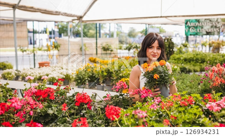 Woman gardener holding potted marigold flowers in greenhouse Woman gardener holding potted marigold flowers in greenhouse 126934231