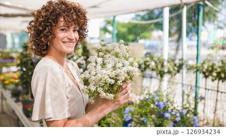 Smiling woman holding white flowers inside garden center Smiling woman holding white flowers inside garden center 126934234