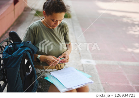 Woman Sorting Documents Outdoors While Preparing for Study or Work Tasks Woman Sorting Documents Outdoors While Preparing for Study or Work Tasks 126934723