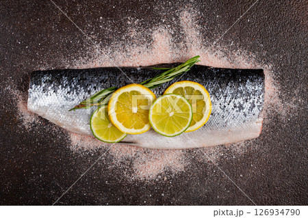 Fresh fish fillet, garnished with lemon and herbs, on a dark background, ready to cook 126934790