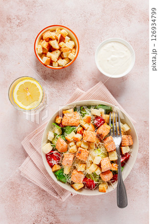 caesar salad with salmon, with croutons and dressing, in a salad bowl, on a pink table, 126934799