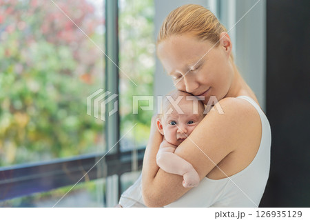 Mother gently hugging her baby at home, sharing a warm and loving moment. Parenthood, family bonding, and maternal love concept 126935129