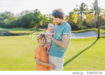 Father, older son, and newborn baby on a meadow in the park. Family spending quality time together in nature. Parenthood, love, and family bond concept Father, older son, and newborn baby on a meadow in the park. Family spending quality time together in nature. Parenthood, love, and family bond concept 126935130