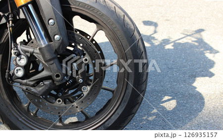 The front wheel of a motorcycle standing on the roadside and its shadow on the asphalt The front wheel of a motorcycle standing on the roadside and its shadow on the asphalt 126935157