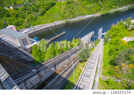 Orlik Dam showcases a boat lift that elevates vessels between levels of water. Surrounded by lush greenery, the structure facilitates navigation along the river. 126935174