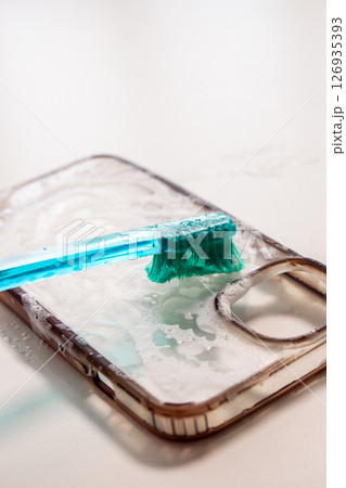 Smartphone case being cleaned with a toothbrush and soap, showcasing a close-up of the cleaning process, highlighting the importance of device maintenance and hygiene practices Smartphone case being cleaned with a toothbrush and soap, showcasing a close-up of the cleaning process, highlighting the importance of device maintenance and hygiene practices 126935393